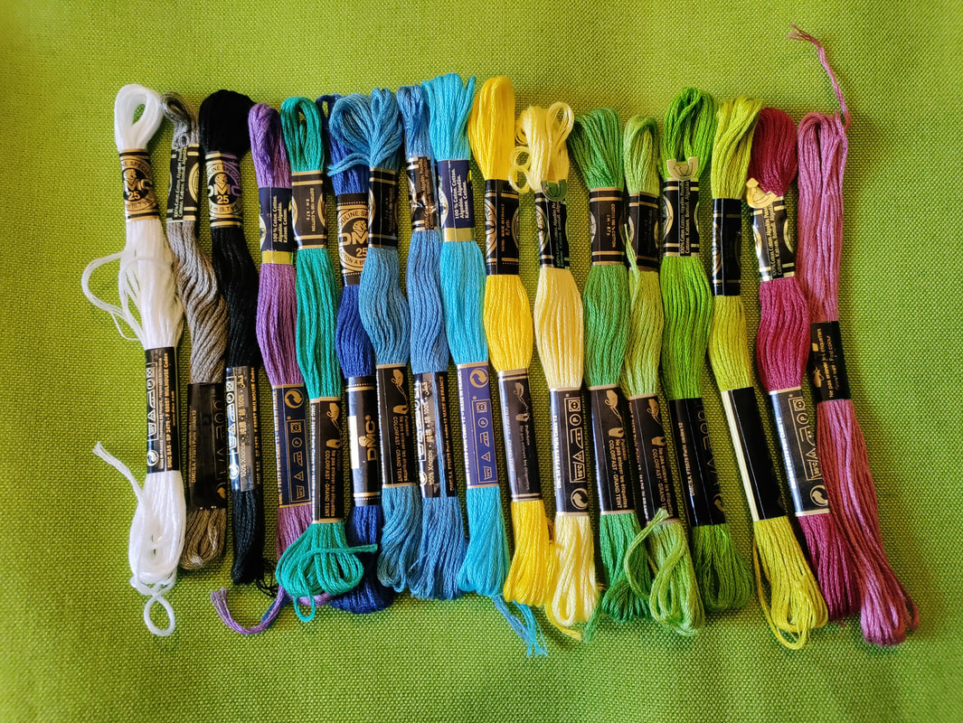 Skeins of embroidery floss in shades of white, grey, black, purple, blue, yellow, green, and pink laid atop a green evenweave fabric